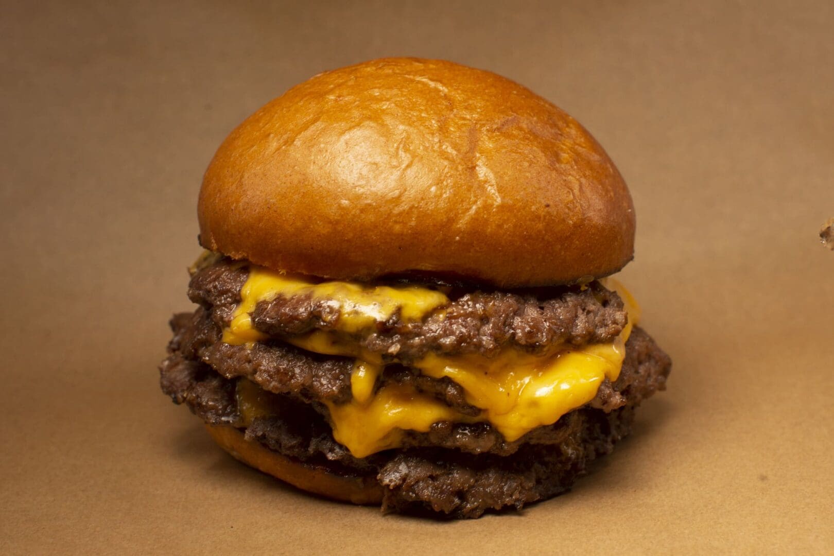 Juicy triple cheeseburger on brown background.