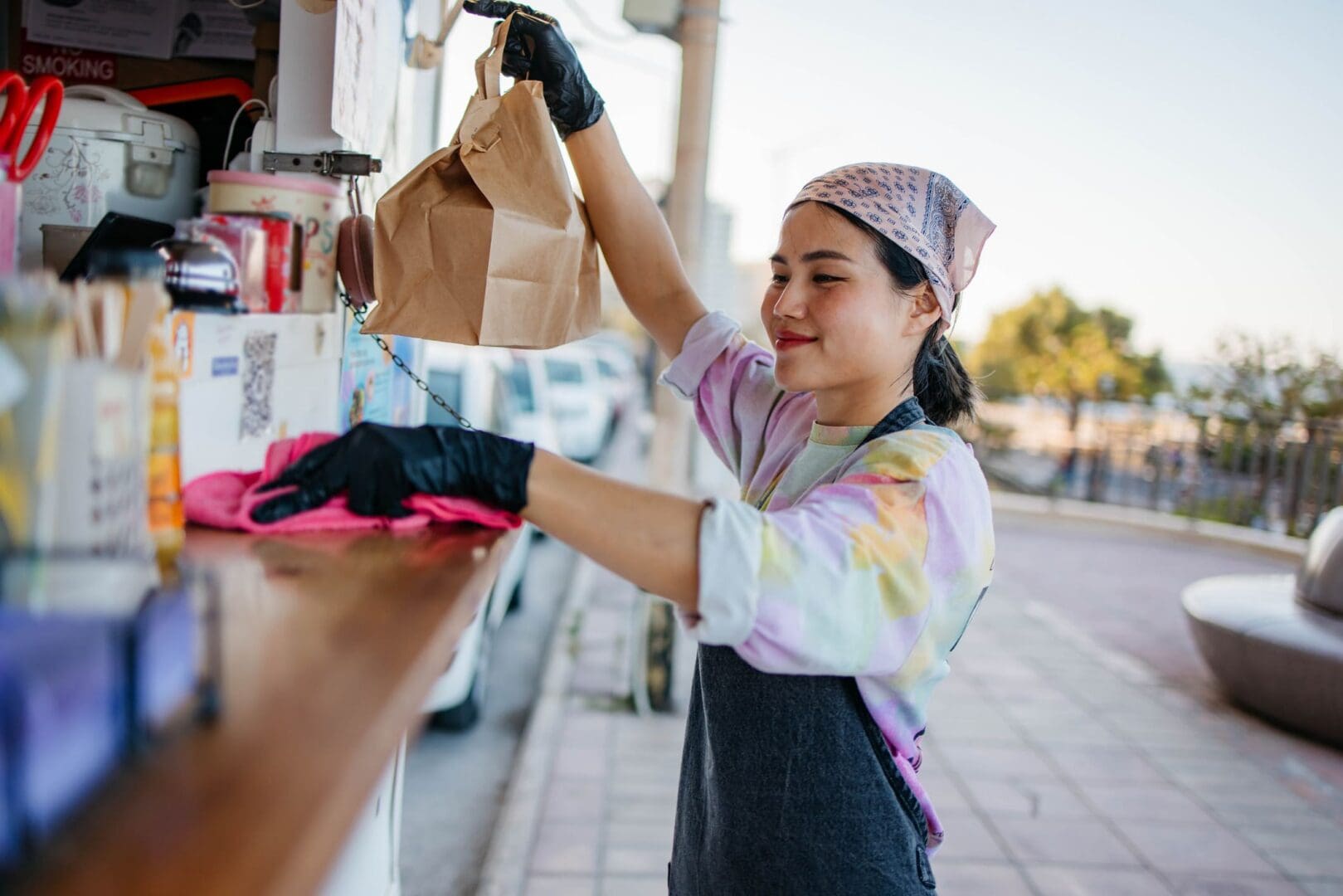 Smiling vendor with takeout bag and gloves.